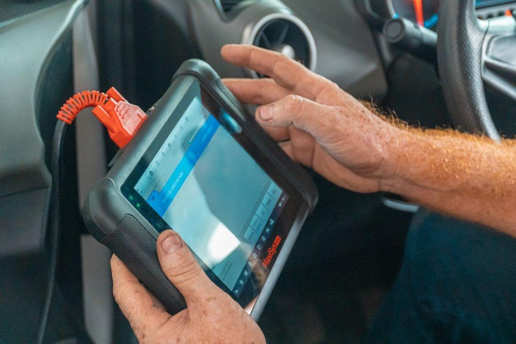 Technician connecting diagnostic equipment to a modern vehicle to perform ADAS calibration during collision repair