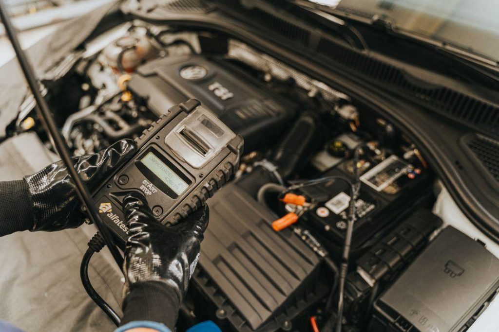 Technician performing battery diagnostics and system scans on a car in a collision repair facility